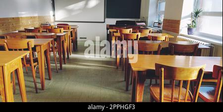 Musik solfeggio leerer Unterricht in der Schule. Die Sonnenstrahlen fallen durch das Fenster auf den Boden. Studententische und -Stühle aus Holz. Schulamt und weiße Wände. Schuleinrichtung. Stockfoto