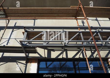 Gerüste auf einem neuen einstöckigen Haus. Die Fassade funktioniert. Geschäftsgebäude. Flaches privates Gebäude. Die Wand eines Gebäudes putzen. Ladenbau. Produktionsstrukturen für Metall. Stockfoto