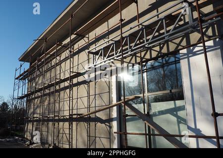 Gerüste auf einem neuen einstöckigen Haus. Die Fassade funktioniert. Geschäftsgebäude. Flaches privates Gebäude. Die Wand eines Gebäudes putzen. Ladenbau. Produktionsstrukturen für Metall. Stockfoto