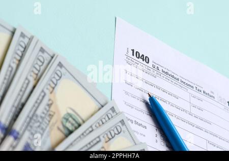 Das Steuerformular für 1040 liegt in etwa 100-Dollar-Scheinen und einem blauen Stift auf hellblauem Hintergrund. US-Einkommensteuererklärung Stockfoto