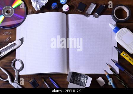 Eine Schule oder Büro Stillleben mit einem offenen Schule Notebook oder Scheckheft und viele Bürobedarf. Das Schulmaterial liegt auf einem braunen Holzhintergrund. Für Text platzieren Stockfoto