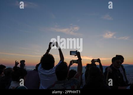 Touristen können die untergehende Sonne über Athen im Frühling auf ihren Mobiltelefonen festhalten Stockfoto