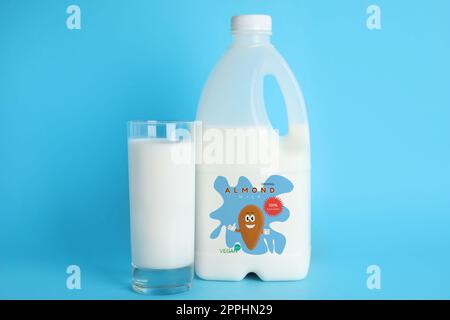 Gallonflasche und Glas Mandelmilch auf hellblauem Hintergrund. Veganes Produkt Stockfoto