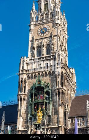 Die neogotische Fassade des neuen Rathauses mit Rathausturm in der Münchner Altstadt im Blick von unten vom Marienplatz bei schönem Sommerwetter und blauem Himmel mit den beiden Türmen der Frauenkirche im Hintergrund Stockfoto