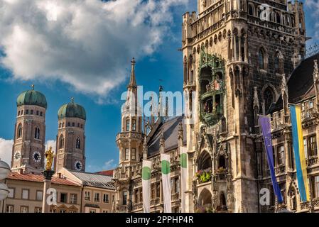 Die neogotische Fassade des neuen Rathauses mit Rathausturm in der Münchner Altstadt im Blick von unten vom Marienplatz bei schönem Sommerwetter und blauem Himmel mit den beiden Türmen der Frauenkirche im Hintergrund Stockfoto