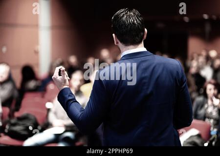Rückansicht des Lautsprechers für einen Vortrag auf einer geschäftlichen Konferenz. Publikum im Konferenzsaal. Veranstaltung für Unternehmen und unternehmerische Initiative. Panorama-Komposition Stockfoto