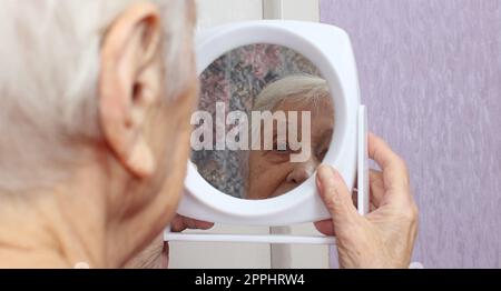 Porträt einer alten Frau, die zu Hause in einen Spiegel schaut Stockfoto