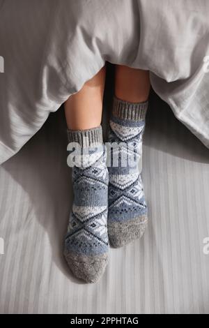 Eine Frau trägt gestrickte Socken unter einer Decke im Bett, Nahaufnahme Stockfoto