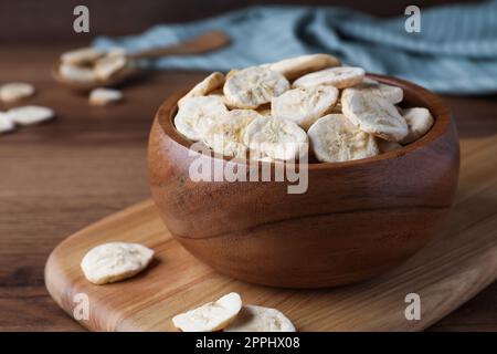 Schüssel und getrocknete Bananenscheiben auf Holztisch, Nahaufnahme Stockfoto