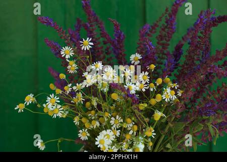 Wunderschöner Blumenstrauß mit Feldblumen in der Nähe einer grünen Holzwand, Nahaufnahme Stockfoto