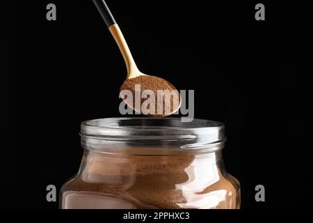 Löffel Instantkaffee über dem Glas vor schwarzem Hintergrund, Nahaufnahme Stockfoto