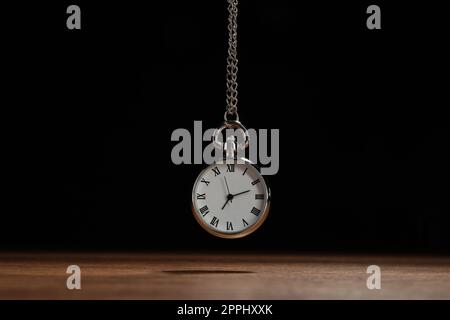 Wunderschöne Taschenuhr im Vintage-Stil mit silberner Kette auf schwarzem Hintergrund über dem Holztisch. Hypnose-Sitzung Stockfoto