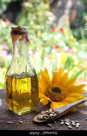 Eine Flasche Sonnenblumenöl und geschälte Samen auf einem Holztisch im Freien Stockfoto