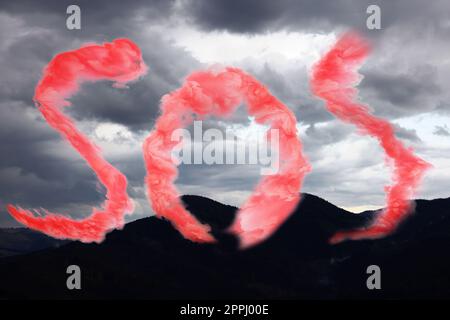 Wort SOS aus rotem Rauch und Blick auf den bewölkten Himmel über den Bergen Stockfoto