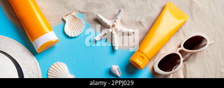 Sommerkomposition mit Sonnencreme-Flaschen, Seesternen, Muscheln und Sonnenbrille auf blauem Hintergrund mit Sand, Banner. Sommerurlaub und Haut ca. Stockfoto