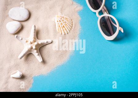 Sommerkomposition mit Kieseln, Seesternen und Muscheln auf blauem Hintergrund mit Sand, Kopierraum. Vorlage für Sommerurlaub und Strandkonzept. Stockfoto