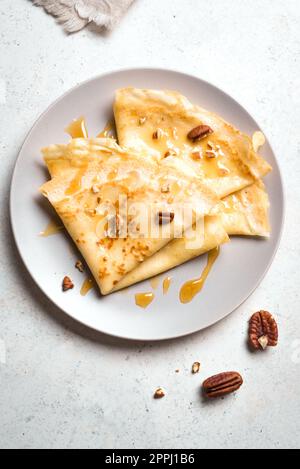 Crepes Suzette mit Honig und Pekannüssen auf weißem Hintergrund. Leckere hausgemachte Crepes zum Frühstück. Stockfoto