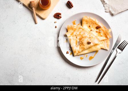 Crepes Suzette mit Honig und Pekannüssen auf weißem Hintergrund. Leckere hausgemachte Crepes zum Frühstück. Stockfoto