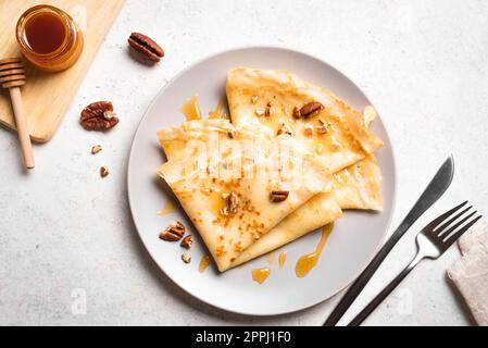 Crepes Suzette mit Honig und Pekannüssen auf weißem Hintergrund. Leckere hausgemachte Crepes zum Frühstück. Stockfoto