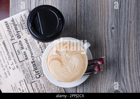 Keramik- und Papptasse Kaffee auf einem Holztisch in der Nähe der Zeitung. Draufsicht. Stockfoto