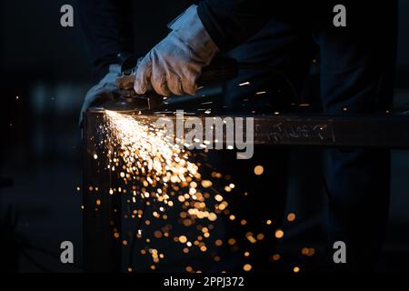 Mann, der mit Schleifmaschine an Eisen arbeitet. Mann bei der Arbeit. Funkelt und Feuer vom Schneiden der Mühle. Mahlwerk. Arbeiter. Stockfoto