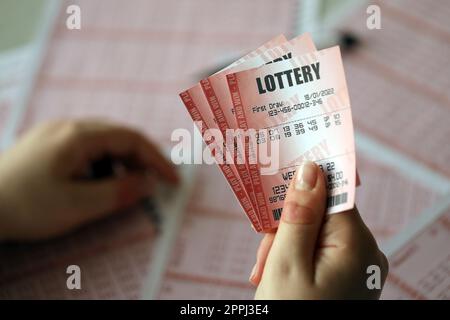 Ein Lotterielos ausfüllen. Eine junge Frau hält das Lotterielos mit einer kompletten Zahlenreihe auf dem Hintergrund der leeren Blätter. Stockfoto