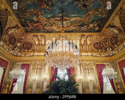 Wunderschön eingerichtete Napoleon Apartments im Louvre Palace. Königliche Familienzimmer mit kardinalroten Vorhängen, goldverzierten Wänden, Gemälden und Kristallkronleuchtern an der Decke Stockfoto