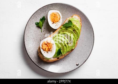 Avocado Toast mit gekochten Eiern auf dem Teller. Getoastetes Brot mit Avocado und Ei für ein gesundes Frühstück, Draufsicht. Stockfoto