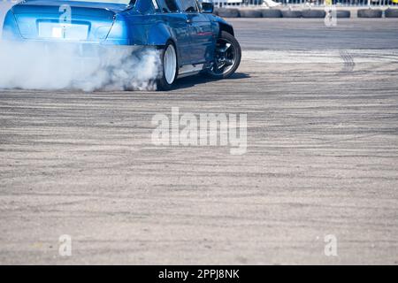 Rückansicht eines blauen Sportwagens, der auf einer Fahrbahn mit grauer Geschwindigkeit abdriftet, wobei Rauch aus dem Hinterrad austritt Stockfoto