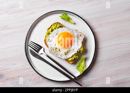 Avocado Toast mit Spiegelei auf Holztisch. Getoastetes Brot mit Avocado und Ei für ein gesundes Frühstück. Stockfoto