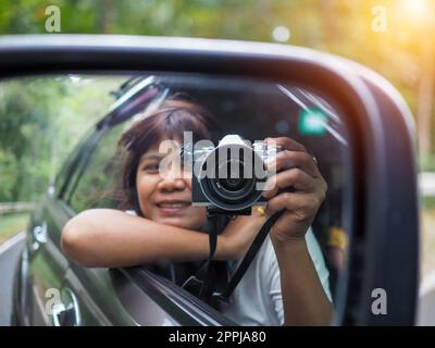 Eine Frau hält eine Digitalkamera in der Hand und macht ein Bild von sich selbst, das im Spiegel reflektiert wird. Stockfoto