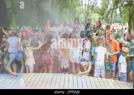 Lemberg, Ukraine - 18. Juli 2021: Color Holi Festival, eine Menschenmenge von Erwachsenen und kleinen Kindern werfen farbenfrohe Farben. Indianerurlaub, Kinder laufen auf einer Holzbühne, schlechte Sicht durch Farbstaub. Stockfoto