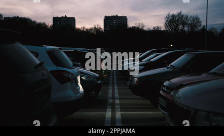 Autos, die in Reihe auf einem Außenparkplatz in Dunkelheit geparkt sind, mit Windstreifen dazwischen Stockfoto