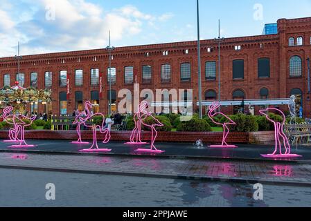 Lodz, Polen - 29. September 2022: Rosa Flamingo-Neonlicht im Brunnen auf dem Innenplatz von Manufaktura bei Sonnenuntergang, ein Kunstzentrum, ein Einkaufszentrum, an Stockfoto