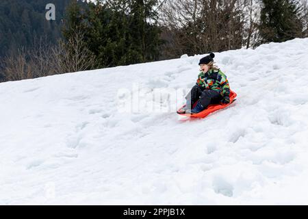 Ein kleines weißes Mädchen, das einen schneebedeckten Hang hinunterschlitten hat. Stockfoto