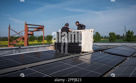 Männliche Teamingenieure, die eigenständige Solarpaneele installieren. Elektriker montieren blaues Solarmodul auf dem Dach eines modernen Hauses. Konzept alternativer Energien Stockfoto