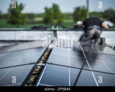 Männliche Teamingenieure, die eigenständige Solarpaneele installieren. Elektriker montieren blaues Solarmodul auf dem Dach eines modernen Hauses. Konzept alternativer Energien Stockfoto