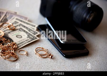 Viele teure goldene Schmuckringe, Ohrringe und Halsketten mit vielen US-Dollar-Scheinen in der Nähe von Smartphones und digitalen spiegelreflexkameras. Pfandhaus Stockfoto