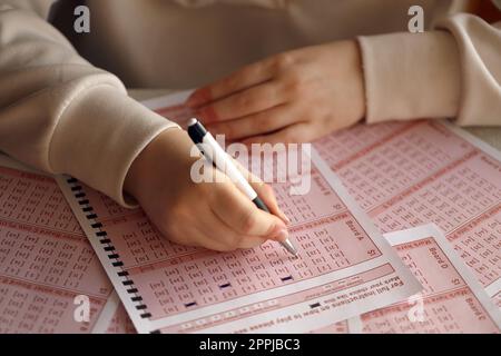 Ein Lotterielos ausfüllen. Eine junge Frau spielt im Lotto und träumt davon, den Jackpot zu gewinnen. Weibliche Handzeichen auf rotem Lotterielos Stockfoto