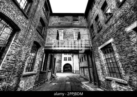 Der Durchgang zwischen zwei Ziegelhäusern im Hinterhof einer Fabrik in Schwarz-Weiß Stockfoto