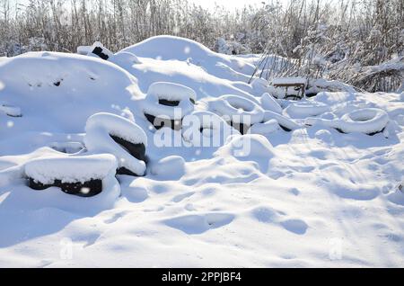 Gebrauchte und entsorgte Autoreifen liegen am Straßenrand und sind mit einer dicken Schneeschicht bedeckt Stockfoto