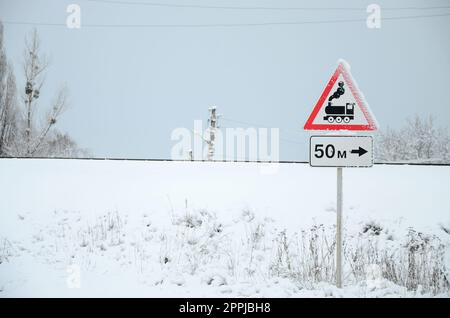 Bahnübergang ohne Barriere. Ein Straßenschild mit einer alten schwarzen Lokomotive in einem roten Dreieck Stockfoto