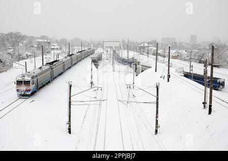 Ein langer Zug von Personenkraftwagen bewegt sich entlang der Eisenbahnstrecke. Eisenbahnlandschaft im Winter nach Schneefall Stockfoto