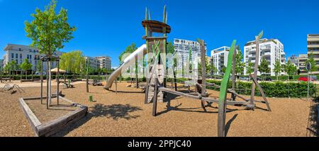 Panoramablick auf Klettergerüste und Spielplatzausstattung auf einem verlassenen Spielplatz mit Apartmentblöcken im Hintergrund Stockfoto