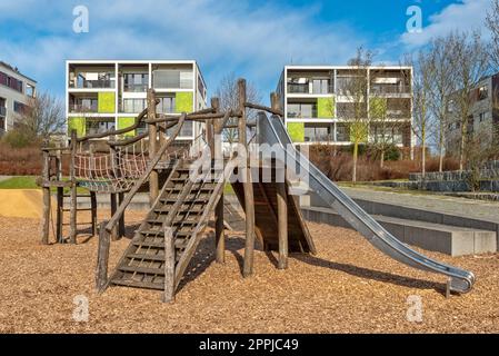 Klettergerüste und Rutschen auf einem verlassenen Spielplatz mit luxuriösen Apartmentgebäuden im Hintergrund Stockfoto