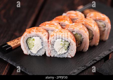 Japanische Küche: Sushi-Brötchen mit Gurke und Frischkäse, garniert mit Shrimps auf schwarzem Brett Stockfoto