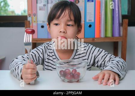 Kinder essen nicht gern Obst. Süßes junges asiatisches Mädchen, das sich weigert, gesunde Früchte zu essen. Ernährung und gesunde Ernährungsgewohnheiten für Kinder. Stockfoto