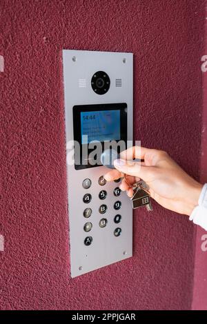 Eine junge Frau gibt den Wohnungscode auf der elektronischen Gegensprechanlage ein, öffnet die Tür mit einer Touch-Taste, dem Bildschirm zur Anzeige von Informationen. Schutz- und Sicherheitskonzept. Stockfoto
