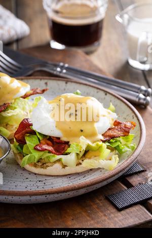 Eggs Benedict mit Speck und Salat auf englischen Muffins mit Hollandaise, traditionelle Frühstücksidee Stockfoto