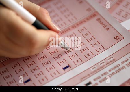 Ein Lotterielos ausfüllen. Eine junge Frau spielt im Lotto und träumt davon, den Jackpot zu gewinnen. Weibliche Handzeichen auf rotem Lotterielos Stockfoto